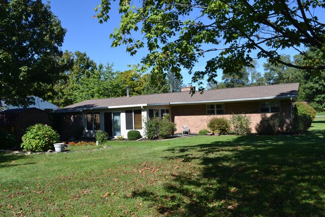 view of front of house featuring a storage shed, a chimney, an outdoor structure, a front lawn, and brick siding