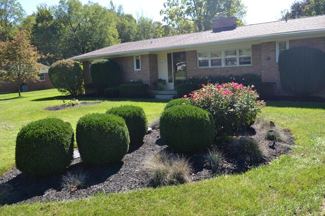 ranch-style home featuring brick siding, a front lawn, and a chimney