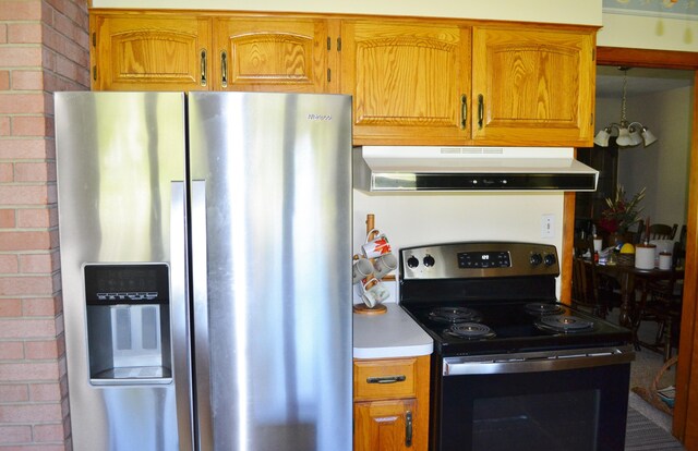 kitchen featuring electric stove, brown cabinetry, brick wall, stainless steel fridge, and under cabinet range hood