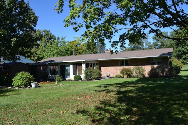 view of front facade with brick siding, a chimney, a storage unit, a front yard, and an outdoor structure