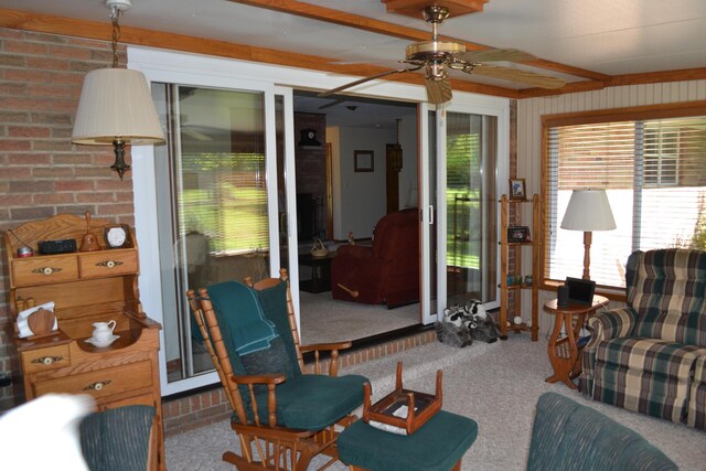 carpeted living area with beam ceiling, ceiling fan, and brick wall