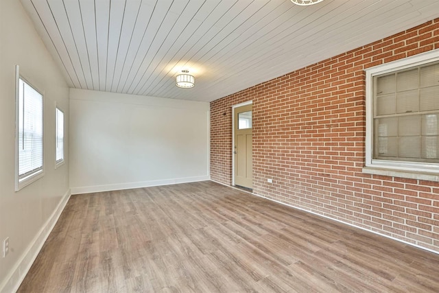 unfurnished room featuring wood ceiling, baseboards, brick wall, and wood finished floors