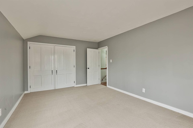 unfurnished bedroom with baseboards, lofted ceiling, a closet, and light carpet