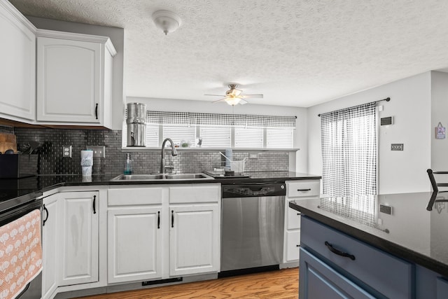 kitchen with a sink, a ceiling fan, white cabinetry, stainless steel dishwasher, and dark countertops
