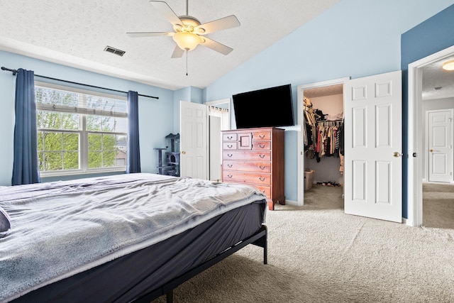 bedroom with carpet flooring, visible vents, vaulted ceiling, a textured ceiling, and a spacious closet