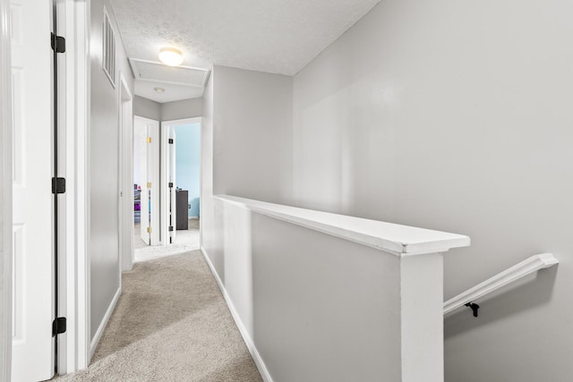 hall featuring attic access, an upstairs landing, carpet flooring, baseboards, and visible vents