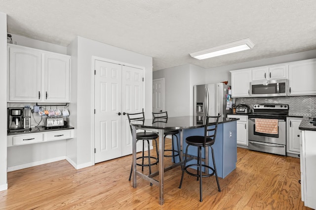 kitchen featuring white cabinetry, dark countertops, stainless steel appliances, a kitchen island, and a kitchen bar