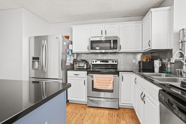 kitchen featuring light wood finished floors, a sink, appliances with stainless steel finishes, and white cabinetry