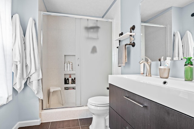 bathroom featuring vanity, toilet, a stall shower, baseboards, and wood finished floors