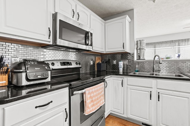 kitchen with decorative backsplash, stainless steel appliances, a sink, white cabinetry, and a textured ceiling