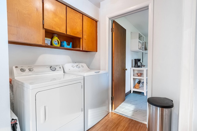 laundry area with separate washer and dryer, light wood-style flooring, and cabinet space
