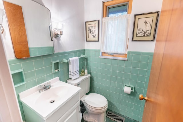 half bath featuring vanity, toilet, a wainscoted wall, tile walls, and visible vents