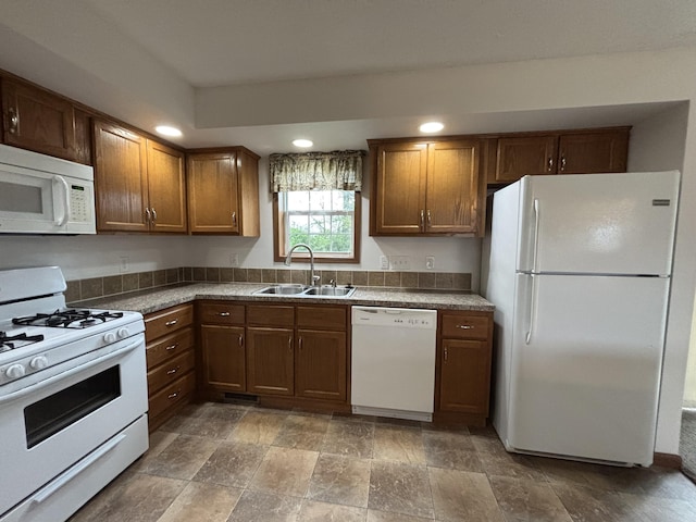 kitchen featuring stone finish floor, brown cabinetry, a sink, recessed lighting, and white appliances