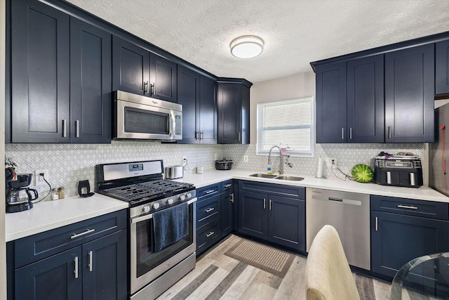 2909 W Barnhill Pl, Xenia, OH 45385 - kitchen featuring appliances with stainless steel finishes, a sink, light wood-style flooring, decorative backsplash, and a textured ceiling