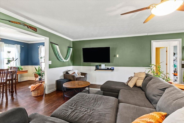 living area with a textured ceiling, crown molding, wood finished floors, and wainscoting