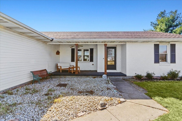 entrance to property with a ceiling fan, brick siding, covered porch, and a shingled roof