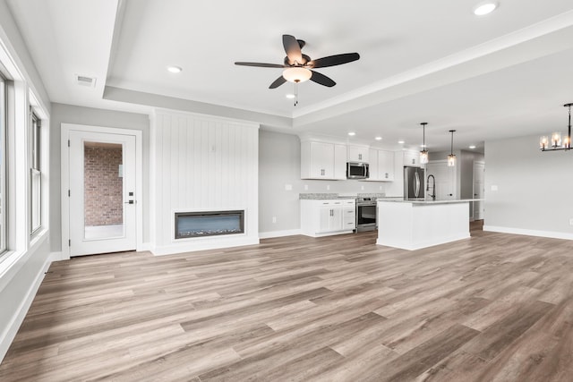 1160 Waterloo St, Troy, OH 45373 - unfurnished living room with ceiling fan, recessed lighting, light wood-style flooring, a tray ceiling, and a large fireplace