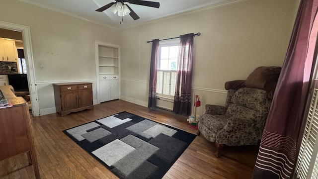 living area featuring built in features, hardwood / wood-style floors, ornamental molding, ceiling fan, and baseboards