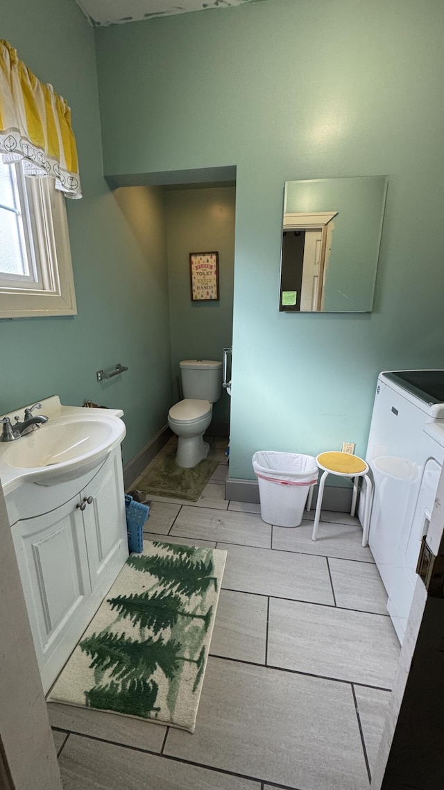 half bathroom with toilet, washing machine and dryer, vanity, and baseboards