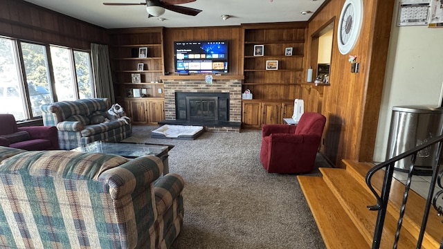 carpeted living room with ceiling fan, wood walls, a fireplace, built in features, and stairs