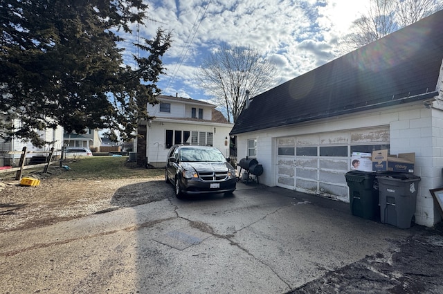 view of property exterior featuring driveway, a garage, concrete block siding, and roof with shingles