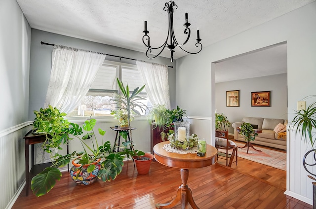 sitting room with a wainscoted wall, a textured ceiling, a chandelier, and wood finished floors