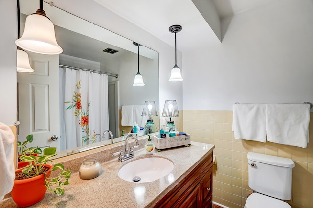 bathroom with toilet, vanity, visible vents, tile walls, and wainscoting