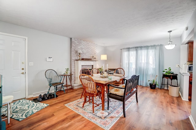 dining area featuring a textured ceiling, light wood finished floors, a fireplace, and baseboards