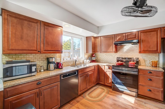 kitchen featuring tasteful backsplash, light wood-style flooring, light stone countertops, stainless steel appliances, and under cabinet range hood