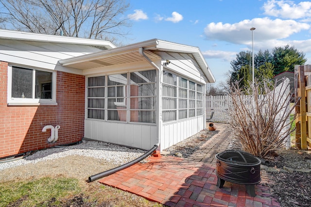 view of home's exterior with brick siding, a sunroom, fence, and a patio