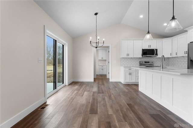 kitchen with decorative light fixtures, dark hardwood / wood-style floors, white cabinets, stainless steel appliances, and backsplash