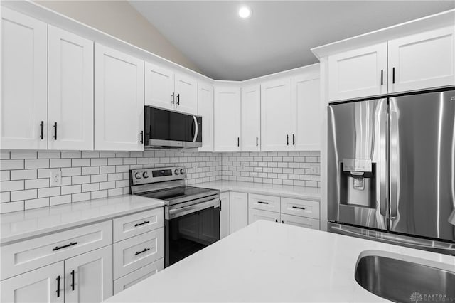 kitchen featuring decorative backsplash, stainless steel appliances, white cabinets, and lofted ceiling
