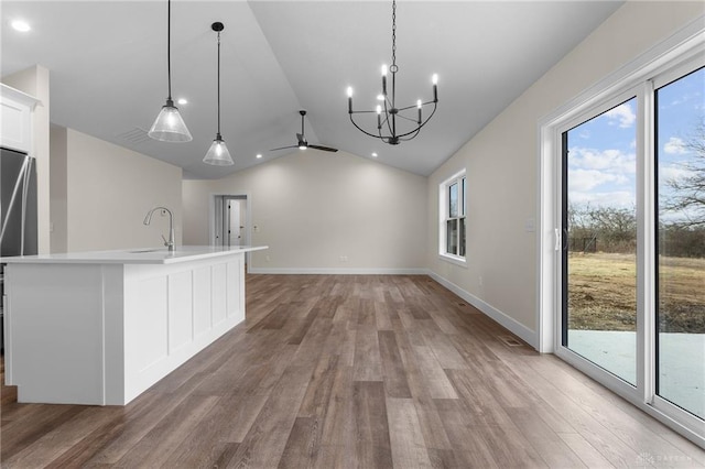 kitchen with lofted ceiling, sink, wood-type flooring, pendant lighting, and a kitchen island with sink