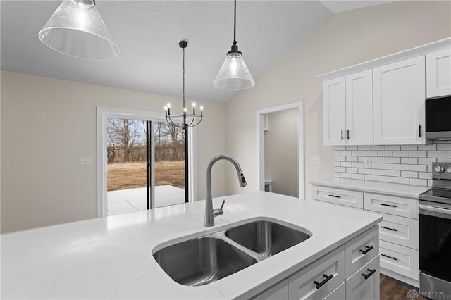kitchen with white cabinets, a sink, stainless steel appliances, decorative light fixtures, and lofted ceiling