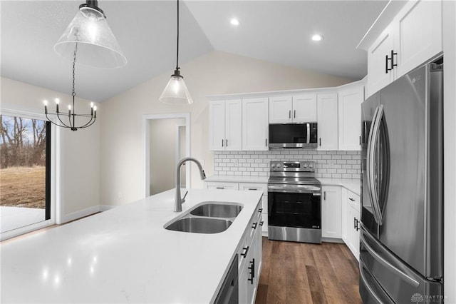 kitchen featuring sink, white cabinetry, stainless steel appliances, decorative light fixtures, and vaulted ceiling