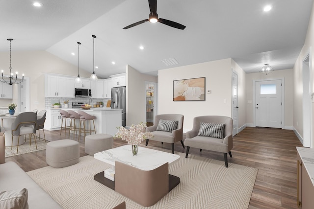 living room with visible vents, wood finished floors, baseboards, ceiling fan with notable chandelier, and vaulted ceiling