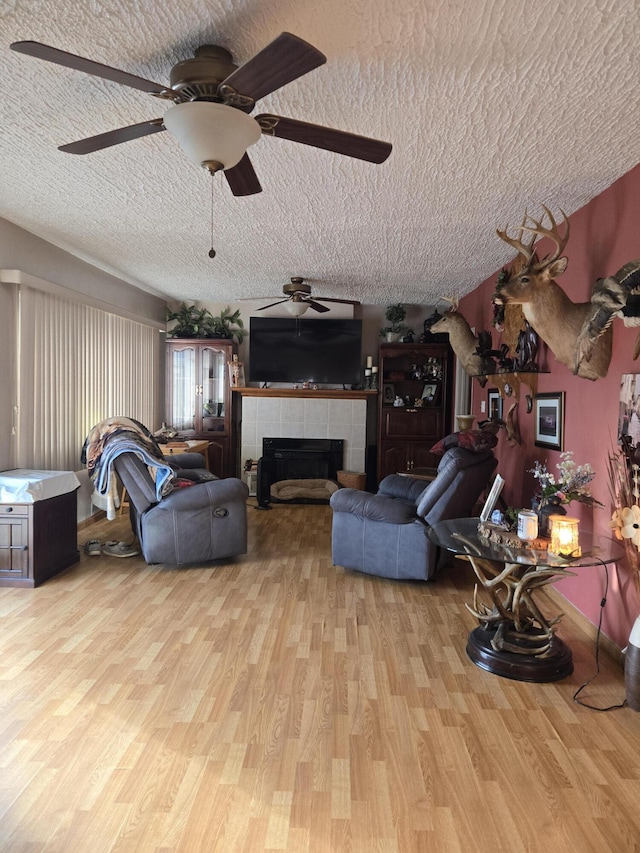 living area with a textured ceiling, wood finished floors, ceiling fan, and a tile fireplace