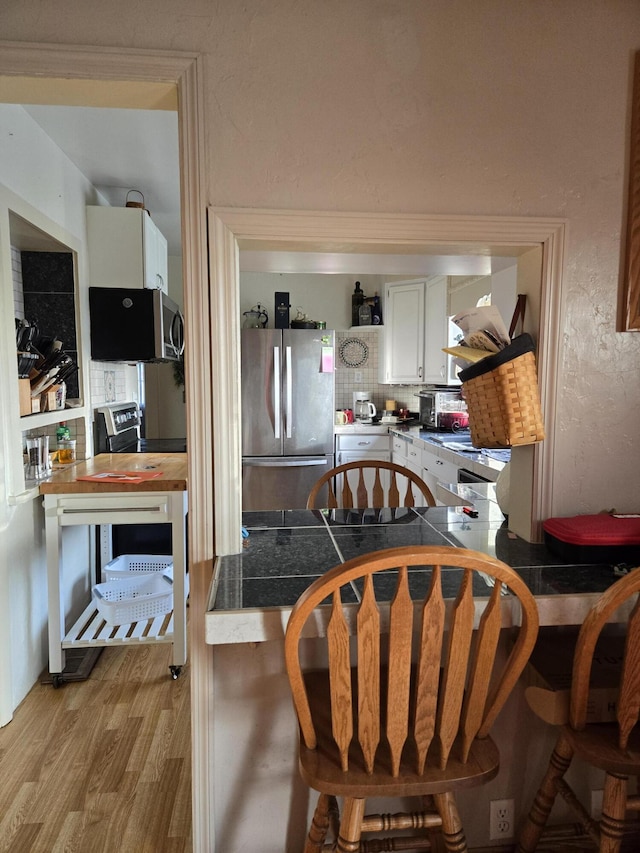 kitchen with white cabinets, a peninsula, a kitchen bar, stainless steel appliances, and light wood-type flooring