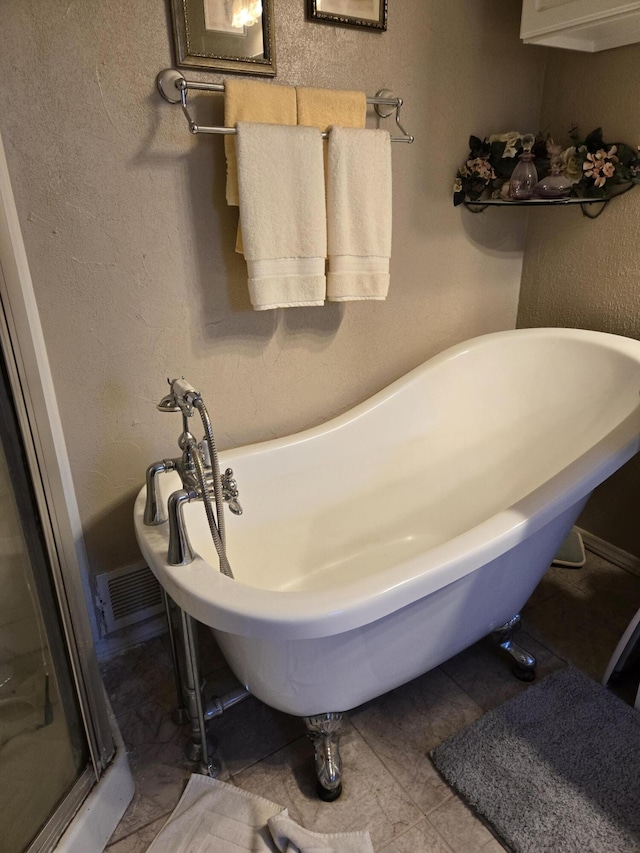 bathroom featuring a freestanding tub, tile patterned floors, visible vents, and a textured wall