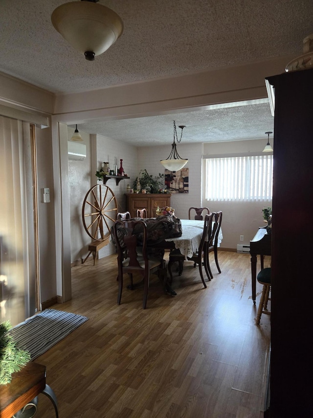 dining space with a wall mounted AC, wood finished floors, and a textured ceiling