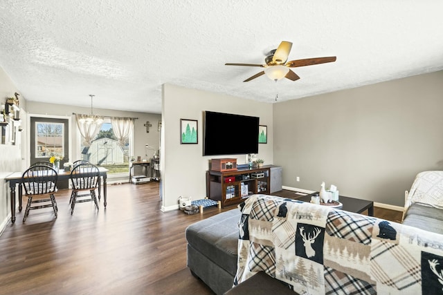 living room with ceiling fan with notable chandelier, a textured ceiling, dark wood-type flooring, and baseboards