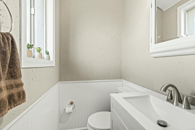 half bath featuring vanity, toilet, and wainscoting