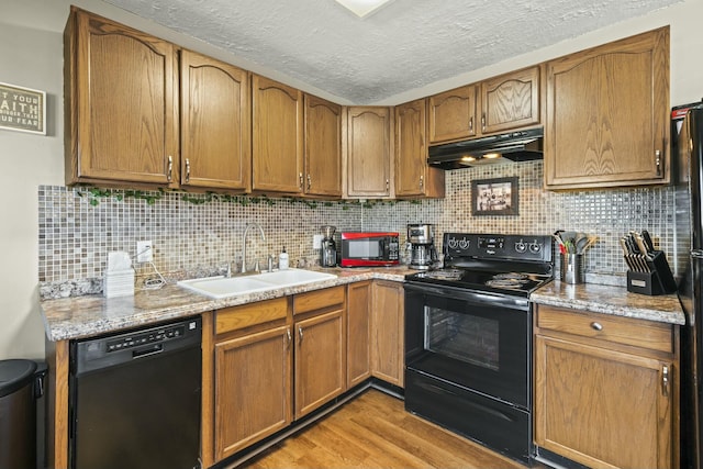 kitchen featuring light wood-style flooring, a sink, black appliances, under cabinet range hood, and backsplash