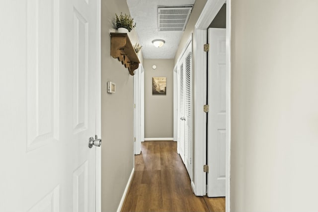 hallway featuring dark wood-style floors, baseboards, visible vents, and a textured ceiling