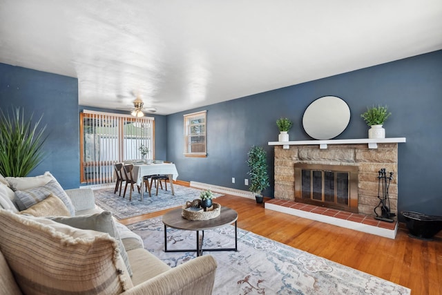 living area with ceiling fan, a fireplace, baseboards, and wood finished floors