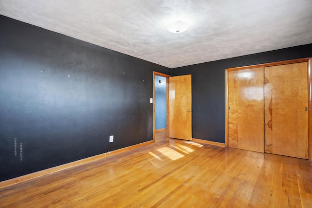 unfurnished bedroom with light wood-type flooring, a closet, and baseboards