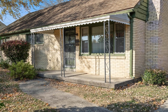 view of property exterior featuring brick siding, a porch, and roof with shingles