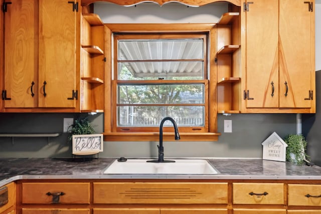 kitchen featuring dark countertops, brown cabinetry, open shelves, and a sink