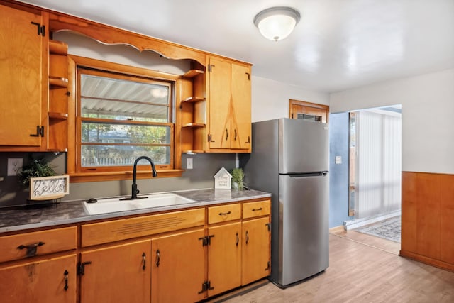 kitchen with brown cabinetry, light wood-style flooring, freestanding refrigerator, open shelves, and a sink