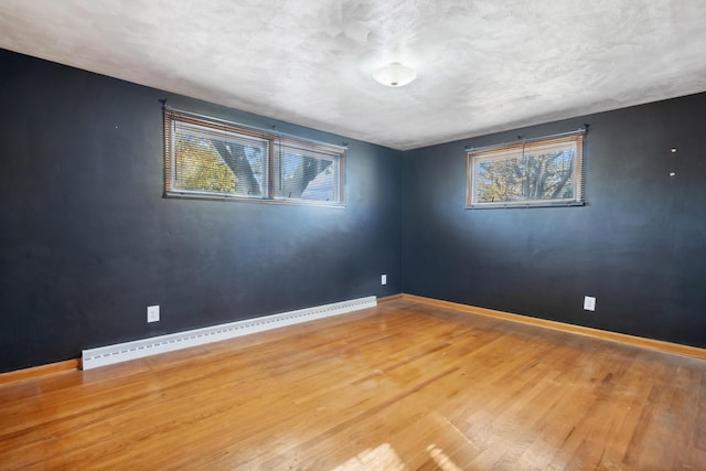 spare room with a baseboard heating unit, wood finished floors, a wealth of natural light, and baseboards